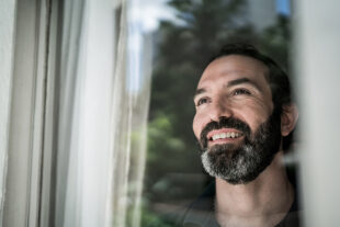 Man looking out the window with hopeful expression